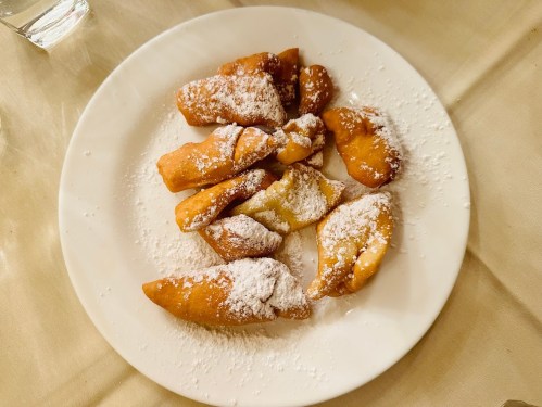 A plate of golden, powdered sugar-dusted pastries arranged neatly.