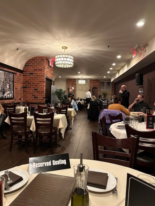 A cozy restaurant interior with reserved seating signs, tables set for dining, and a musician performing in the background.