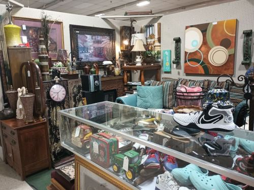 A cozy antique shop filled with furniture, decor, and various items, including shoes and toys displayed in a glass case.