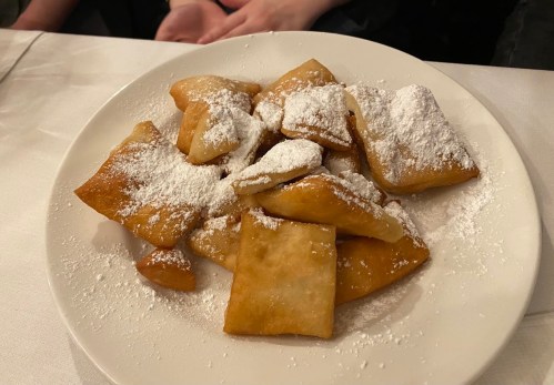 A plate of powdered sugar-dusted pastries, arranged in a casual pile on a white plate.