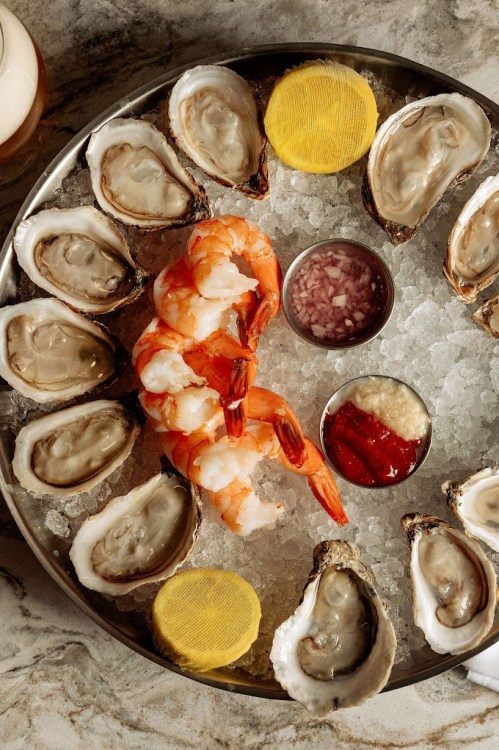 A seafood platter featuring oysters, shrimp, and dipping sauces on a bed of ice.