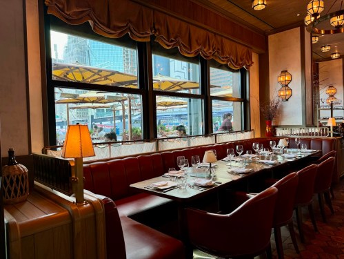 A cozy restaurant interior with a long table set for dining, large windows overlooking an outdoor patio.