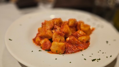 A plate of gnocchi in a rich tomato sauce, garnished with herbs, served on a white dish.