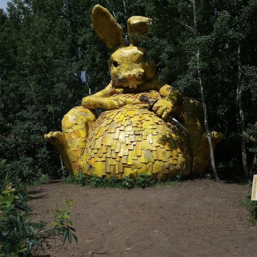 A large, yellow rabbit sculpture made of various materials, surrounded by trees in a natural setting.