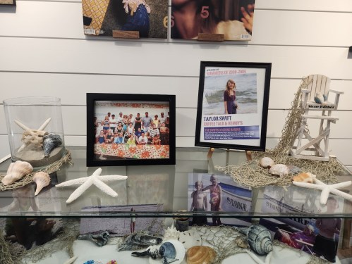 A display featuring seashells, a family photo, and a framed poster of Taylor Swift at a beach-themed setting.