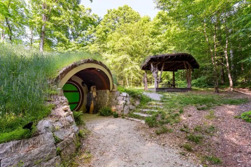 A unique, round entrance to a home surrounded by greenery, with a stone path leading to a gazebo in a wooded area.