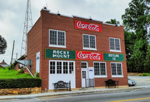 Historic brick building with Coca-Cola signage, labeled "Rocky Mount Bottling Co," surrounded by greenery.