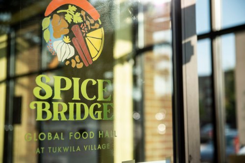 Sign for Spice Bridge, a global food hall at Tukwila Village, featuring colorful food illustrations.