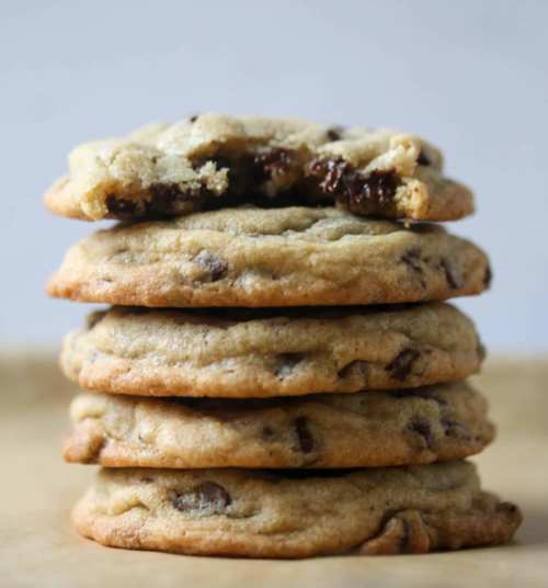 A stack of chocolate chip cookies, with one cookie partially bitten, revealing gooey chocolate inside.