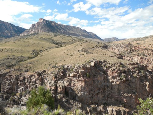 A scenic view of rugged mountains and grassy hills under a partly cloudy sky.