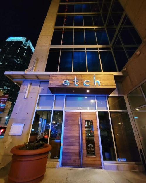 Exterior of the restaurant "etch," featuring a wooden sign and large glass windows, illuminated at night.