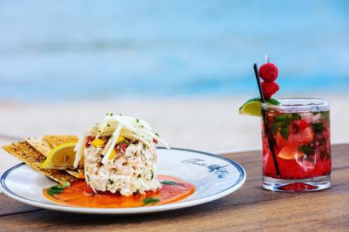 A plate of crab salad with tortilla chips and a refreshing cocktail garnished with raspberries and lime, by the beach.