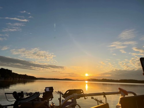 A serene sunset over a calm lake, with clouds reflecting warm colors in the sky and silhouettes of trees in the distance.