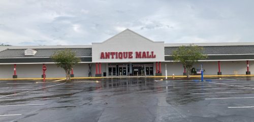 Exterior of an Antique Mall with a large sign, surrounded by a wet parking lot under a cloudy sky.