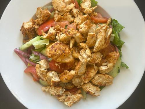 A plate of seasoned, shredded chicken atop a fresh salad with tomatoes, cucumbers, and lettuce.