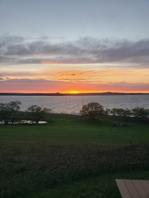 A serene sunset over a lake, with vibrant orange and purple hues in the sky and green grass in the foreground.