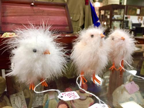 Three fluffy, white decorative chicks with orange beaks and feet, displayed on a wooden surface.