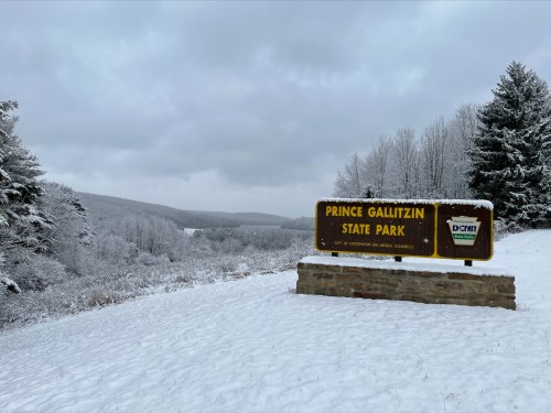 Sign for Prince Gallitzin State Park surrounded by a snowy landscape and overcast skies.