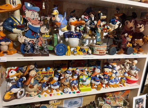 A display of various Donald Duck figurines and collectibles on shelves, showcasing different styles and designs.