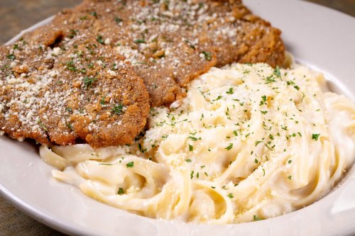 A plate of creamy fettuccine alfredo topped with parsley, accompanied by two breaded chicken cutlets.