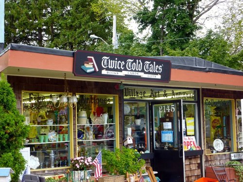 A quaint shop front with a sign reading "Twice Told Tales," featuring books, gifts, and antiques in the windows.