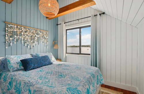 Cozy bedroom with blue walls, a patterned quilt, and a large window showcasing a scenic view.