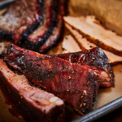 Close-up of various smoked meats, including brisket and ribs, arranged on parchment paper.