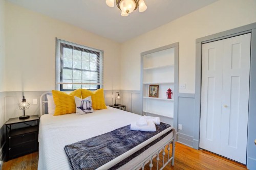 Cozy bedroom with a white bed, yellow pillows, and a bookshelf, featuring warm wood floors and natural light.