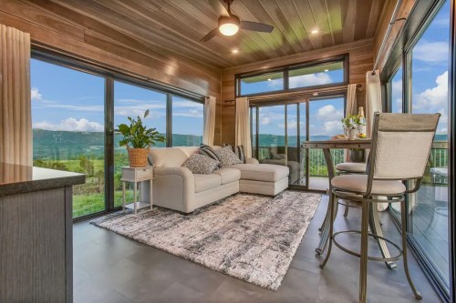 Cozy living space with a sofa, dining area, and large windows showcasing a scenic view of hills and blue sky.
