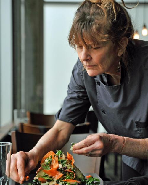 A chef carefully garnishes a colorful salad in a restaurant setting.