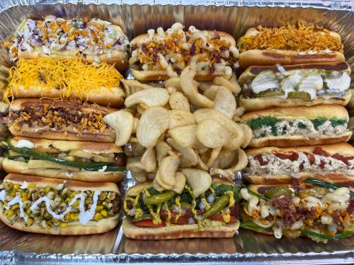 A tray of assorted hot dogs topped with various ingredients, surrounded by crispy potato chips.