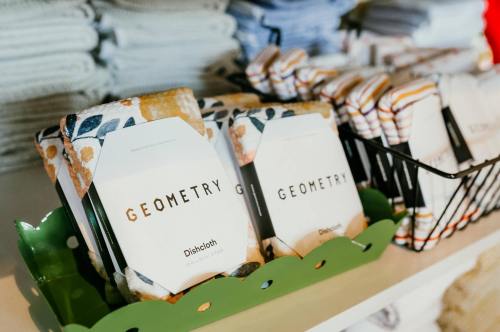A display of colorful dishcloths labeled "GEOMETRY" in a green basket, with neatly stacked towels in the background.