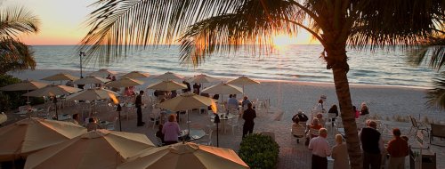 A beachside scene at sunset with people gathered under umbrellas, enjoying the view of the ocean.