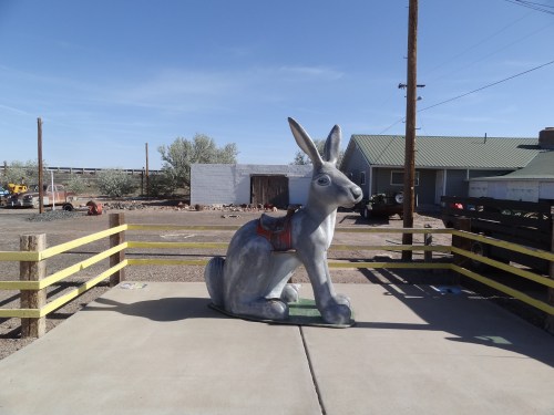A large gray rabbit statue sits on a concrete platform, surrounded by a wooden fence and a rural landscape.