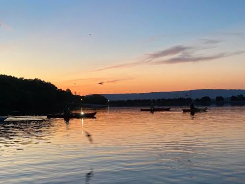 Three kayakers paddle on a calm lake at sunset, with vibrant colors reflecting on the water's surface.