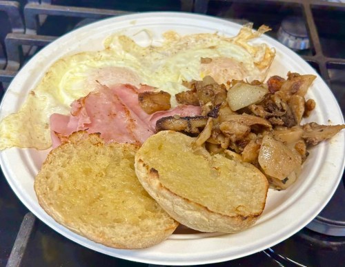 A plate with two fried eggs, ham, sautéed potatoes and onions, and two toasted bread halves.