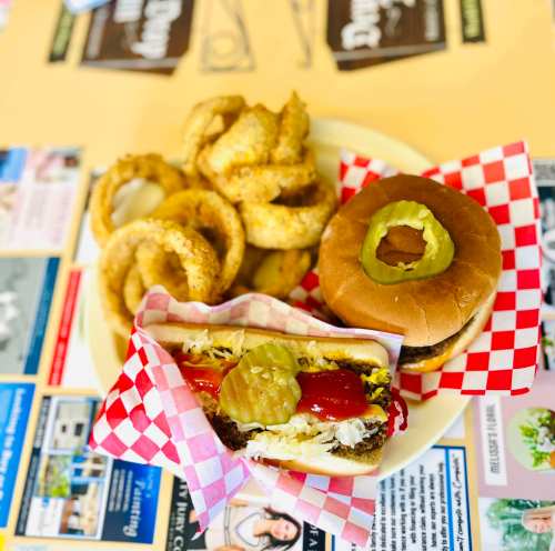 A plate with a cheeseburger topped with pickles and a hot dog with ketchup, alongside a serving of onion rings.