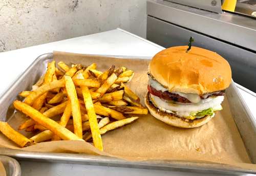A burger with lettuce, tomato, and onion sits on a tray next to a serving of golden French fries.