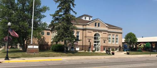 Historic building with a large front entrance, surrounded by trees and a clear blue sky. American flag visible.