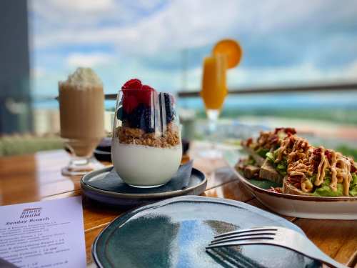 A brunch table featuring yogurt parfait, avocado toast, and drinks with a scenic view in the background.
