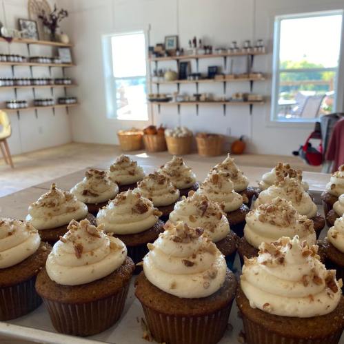 A close-up of cupcakes with cream frosting and nuts, set in a cozy room with shelves and baskets in the background.