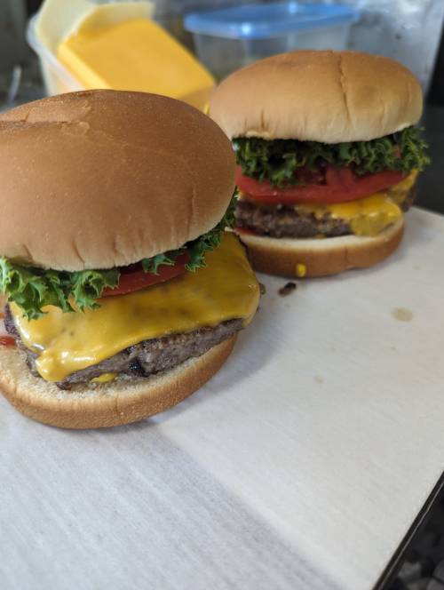 Two cheeseburgers with lettuce, tomato, and melted cheese on soft buns, placed on a white surface.