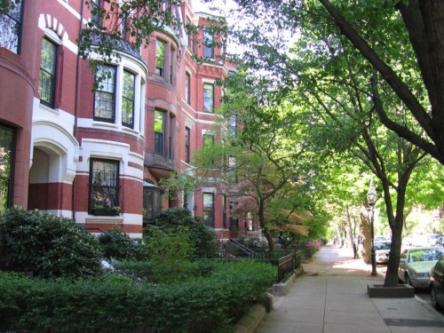 A tree-lined street featuring red brick buildings and lush greenery on a sunny day.