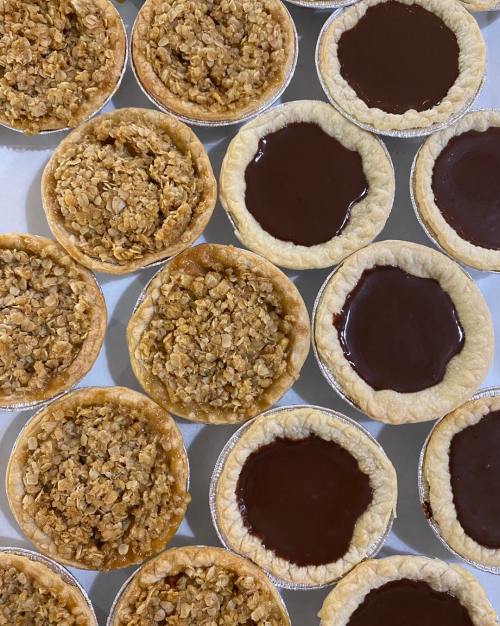 A close-up of mini pies: some with chocolate filling and others topped with oat crumble, arranged in a grid.