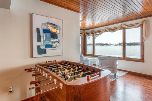 A foosball table in a bright room with large windows overlooking a lake, featuring modern decor and wooden accents.