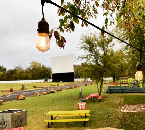 Outdoor movie setup with string lights, a large screen, and colorful picnic tables in a grassy area.