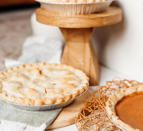 Two pies on wooden stands, one with a lattice crust and the other with a smooth filling, on a textured surface.