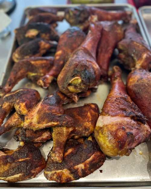 A tray of smoked and charred chicken legs and thighs, showcasing a rich, dark brown color and crispy texture.