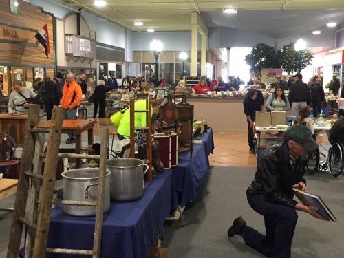 A bustling indoor market with vendors and shoppers, featuring antiques and various items for sale.