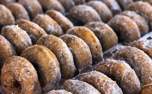 A close-up of freshly made, sugar-coated donuts arranged in a tray.